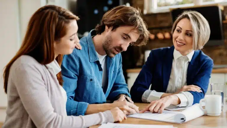 Couple signing home loan documents with a smiling real estate agent explaining the USDA loan process.